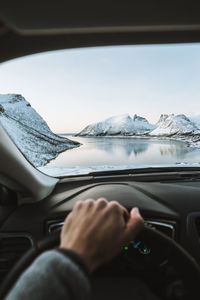 Midsection of person driving car on snowcapped mountains