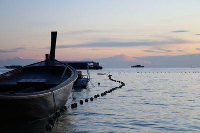 Boat moored in sea against sky during sunset