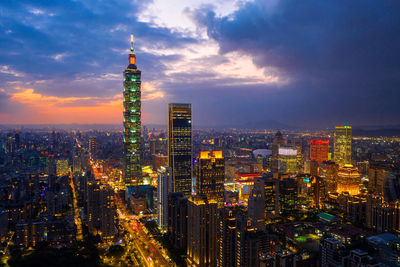 Illuminated buildings in city against cloudy sky