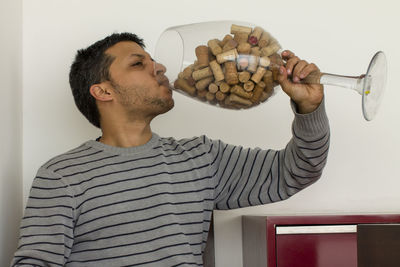 Man drinking cork stoppers from wineglass against wall