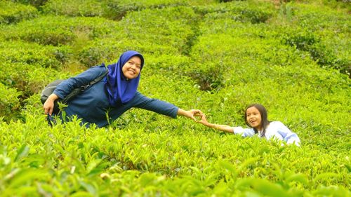 Portrait of smiling mother and girl making heart with hands while standing between tea crops