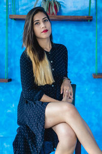 Beautiful young woman sitting against blue wall