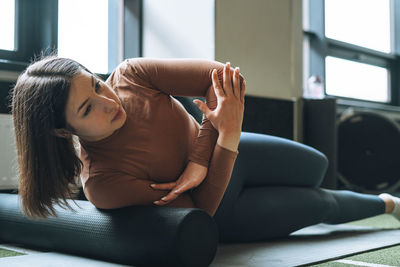 Young brunette woman doing stretching pilates on the massage roll in fitness club gym