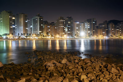 River by illuminated buildings against sky at night