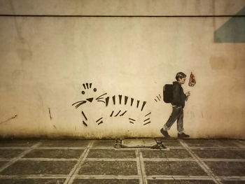 Man walking on footpath against graffiti wall