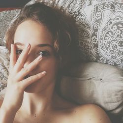 Portrait of woman covering face with hand while relaxing on bed at home