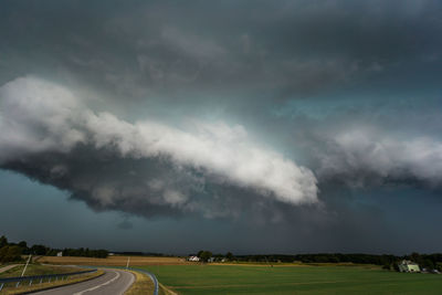 Road passing through field against storm clouds