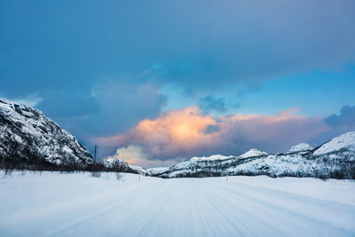 Snow covered landscape against sky during sunset