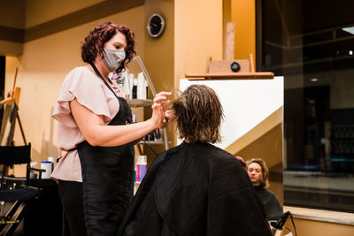 Female hairdresser with face mask hairdressing of young woman in salon