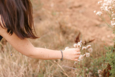 Midsection of woman picking flower on field