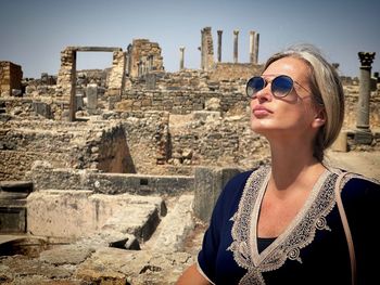 Portrait of young woman wearing sunglasses while standing against old ruins