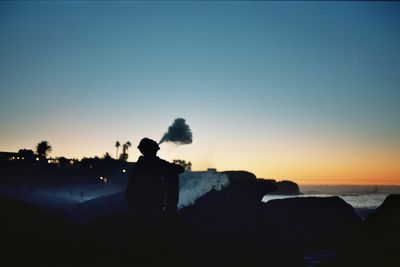 Silhouette man emitting smoke from mouth against clear sky during sunset