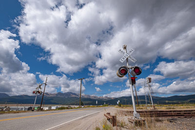 Railroad crossing sign against cloud-sky and rocky mountains in colorado, usa