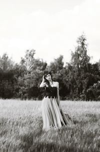 Portrait of woman standing amidst grassy field against sky