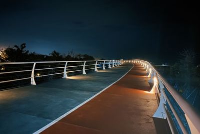 Illuminated bicycle lane bridge against sky at night