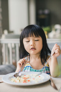 Girl with eyes closed sitting at dining table