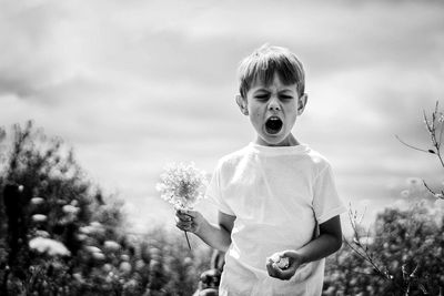 Cute boy standing on field against sky