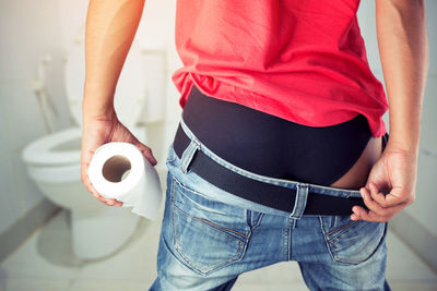 Midsection of man with toilet paper standing in bathroom