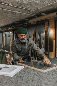 Mature craftsman positioning glass in frame at workbench