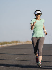 Full length of woman running on road against sky