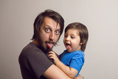 Father in the gray shirt holding a son in a blue t-shirt in the hands of a white wall