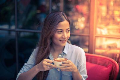 High angle view of thoughtful young woman holding coffee cup in cafe
