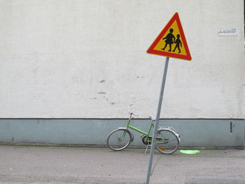 Bicycle parked by information sign against wall