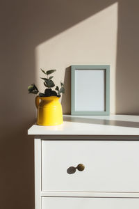 Empty white photo frames on the white table in the interior with beige walls near window.