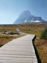 Boardwalk towards mountains against clear sky