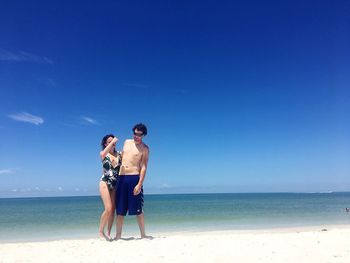 Couple standing at beach against blue sky