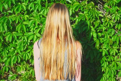Rear view of woman with blond hair standing against plants