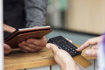 Cropped image of customer paying through card reader while owner using digital tablet at food truck