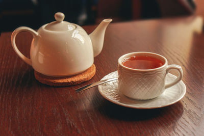 White cup with teapot. pot standing on saucer on naturally blurred background. coffee, tea house