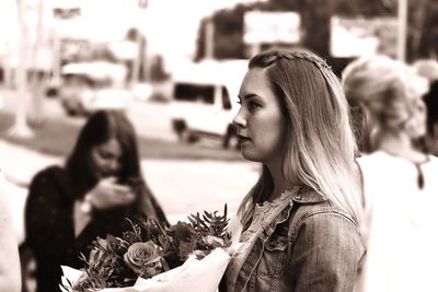 Side view of young woman with bouquet standing on footpath