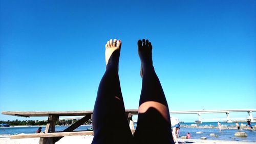 Low section of women relaxing at sea against clear blue sky