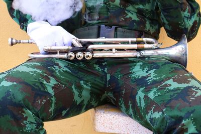 Midsection of army solider with trumpet sitting against wall