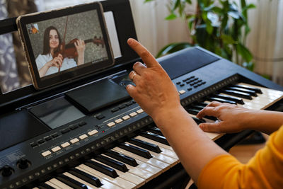 Midsection of woman playing piano while video conferencing over digital tablet at home