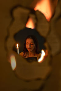 Girl reading book in candle light through flames in dark room