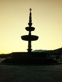 Silhouette cross by street against sky during sunset