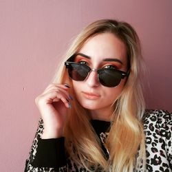Portrait of young woman wearing sunglasses sitting against wall