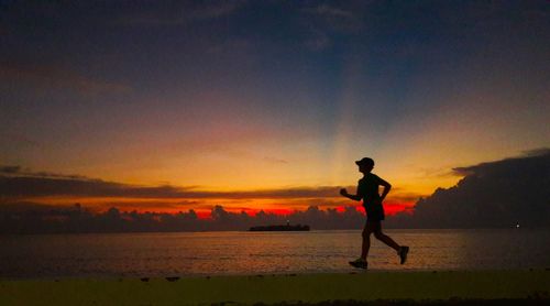 Silhouette man on beach against sky during sunset