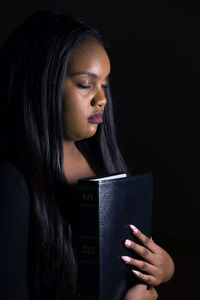 Close-up of young woman reading book against black background