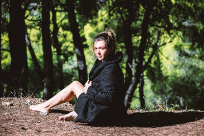 Young woman sitting on tree trunk in forest