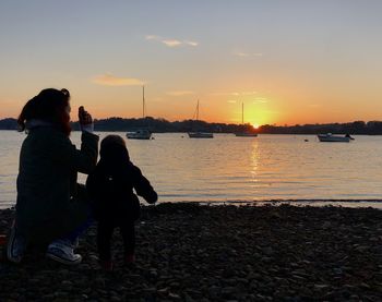 Rear view of women on beach against sky during sunset