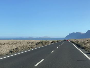 Road passing through landscape against clear blue sky