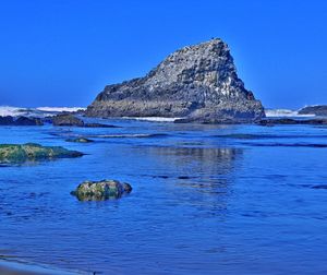 Scenic view of rocks in sea against clear blue sky