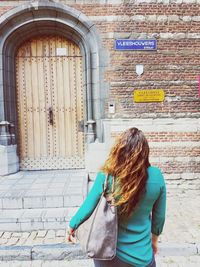 Rear view of woman standing against brick wall