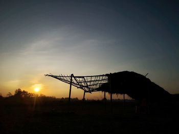 Silhouette cranes on field against sky during sunset