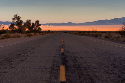 Road amidst trees against sky during sunset