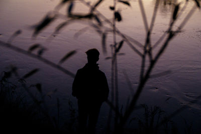 Silhouette man standing by lake at sunset
